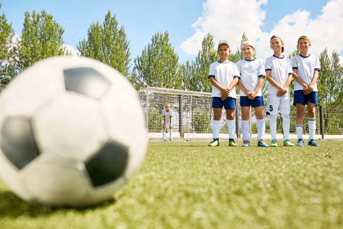 A group of young people standing in front of a soccer ball.